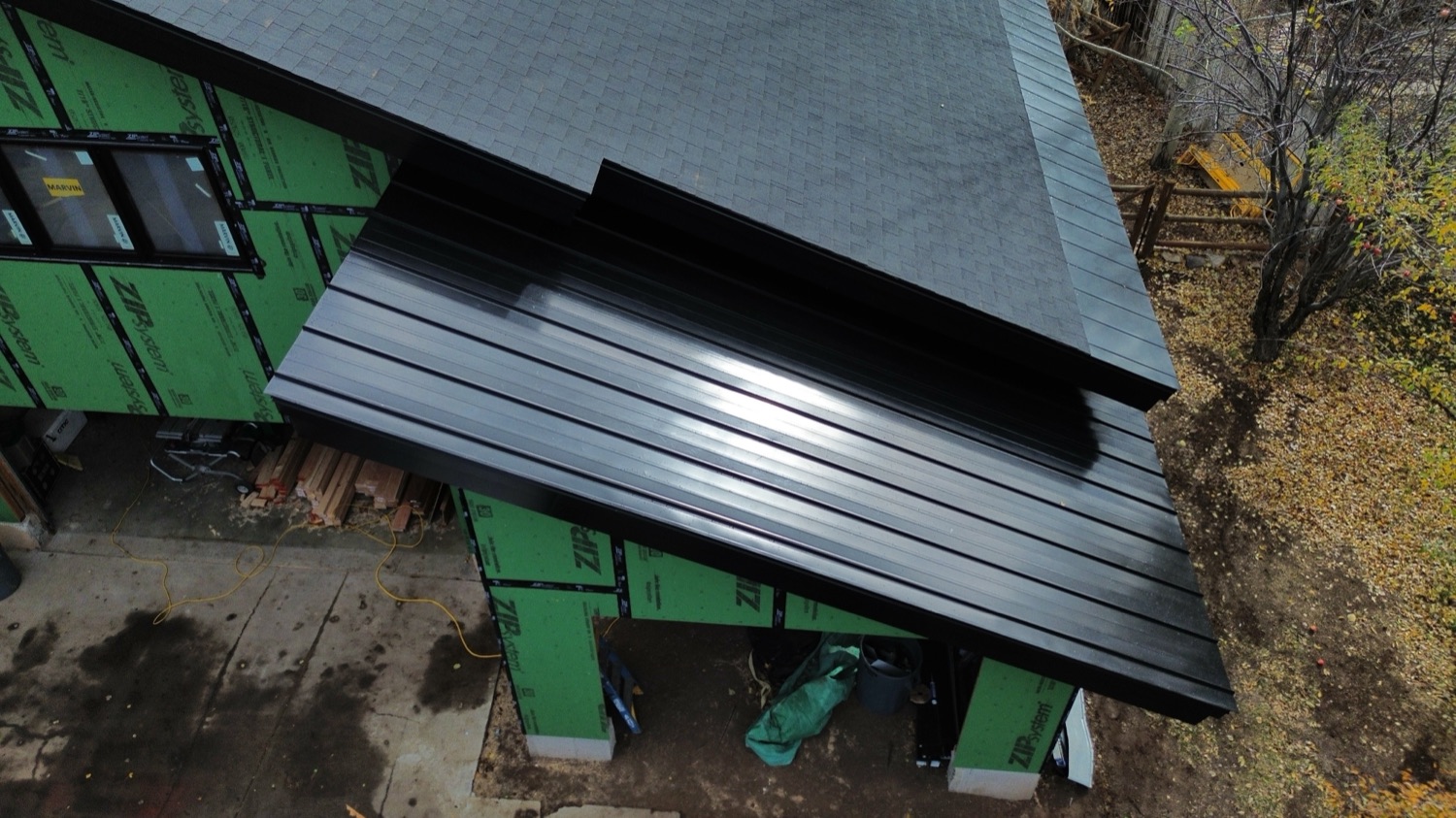 Black standing seam metal roof meeting an architectural shingle section